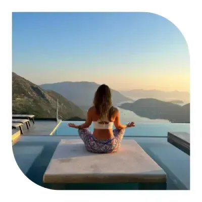 Woman meditating by an infinity pool overlooking mountains and a lake at sunrise, sitting in a peaceful yoga pose.
