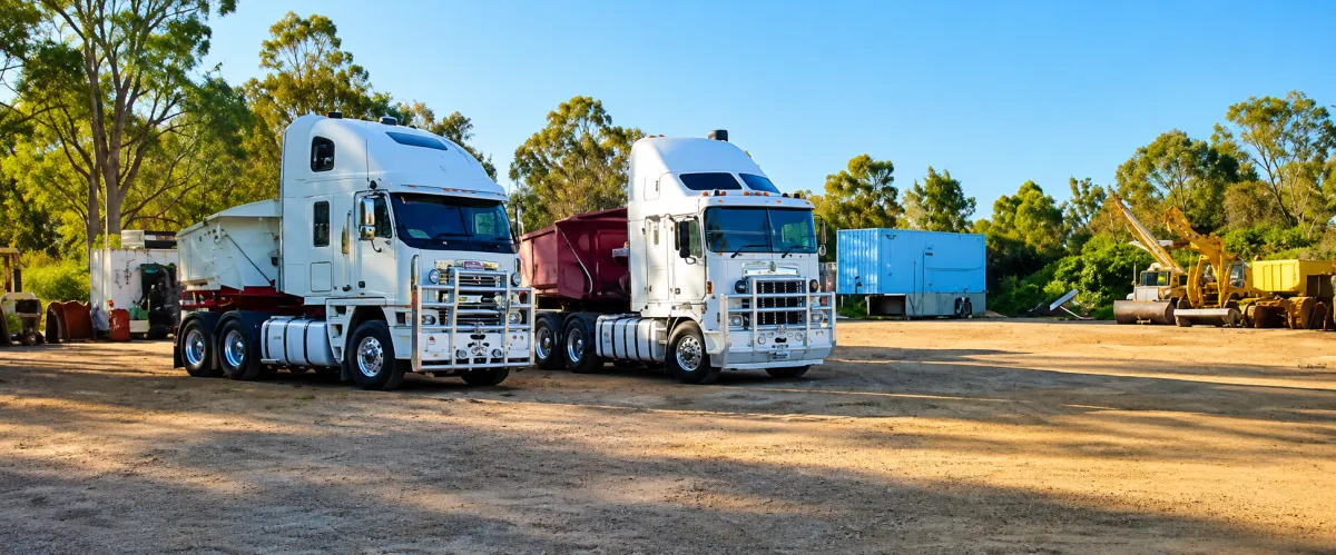 Large transport vehicles including B-Doubles and prime movers parked safely in an expansive industrial lot.