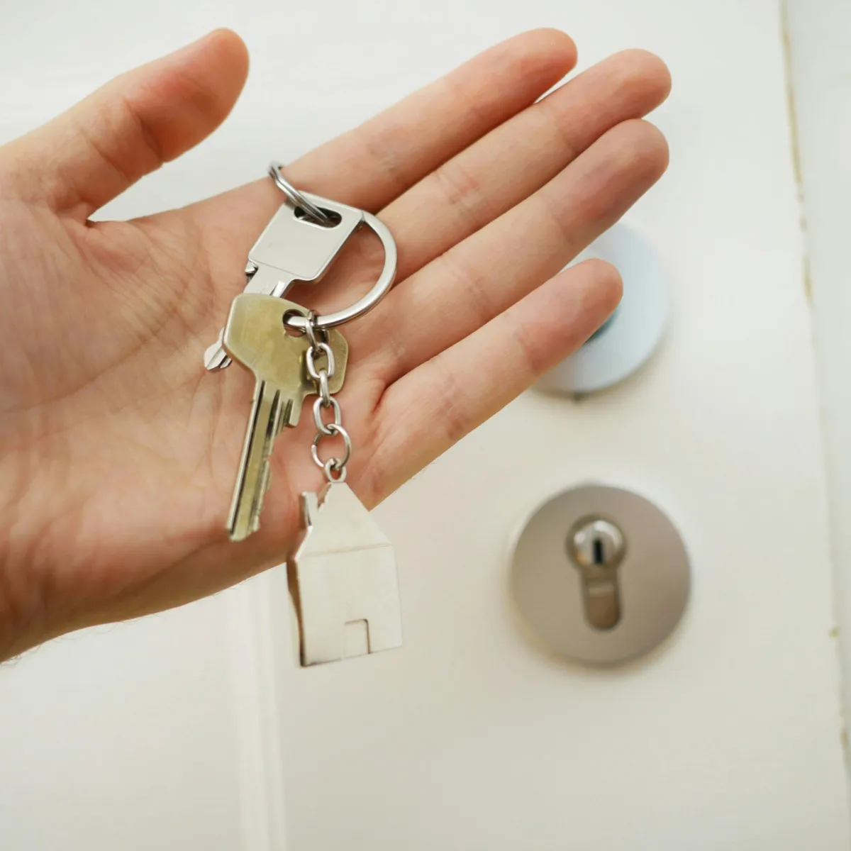 A hand holding front door keys in front of a white door
