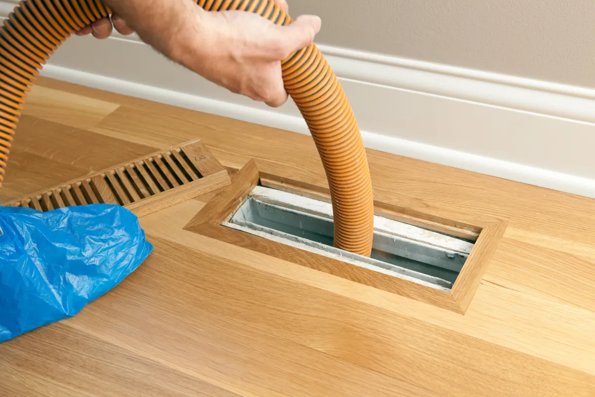 Technician cleaning air duct vents in a residential home for improved air quality.