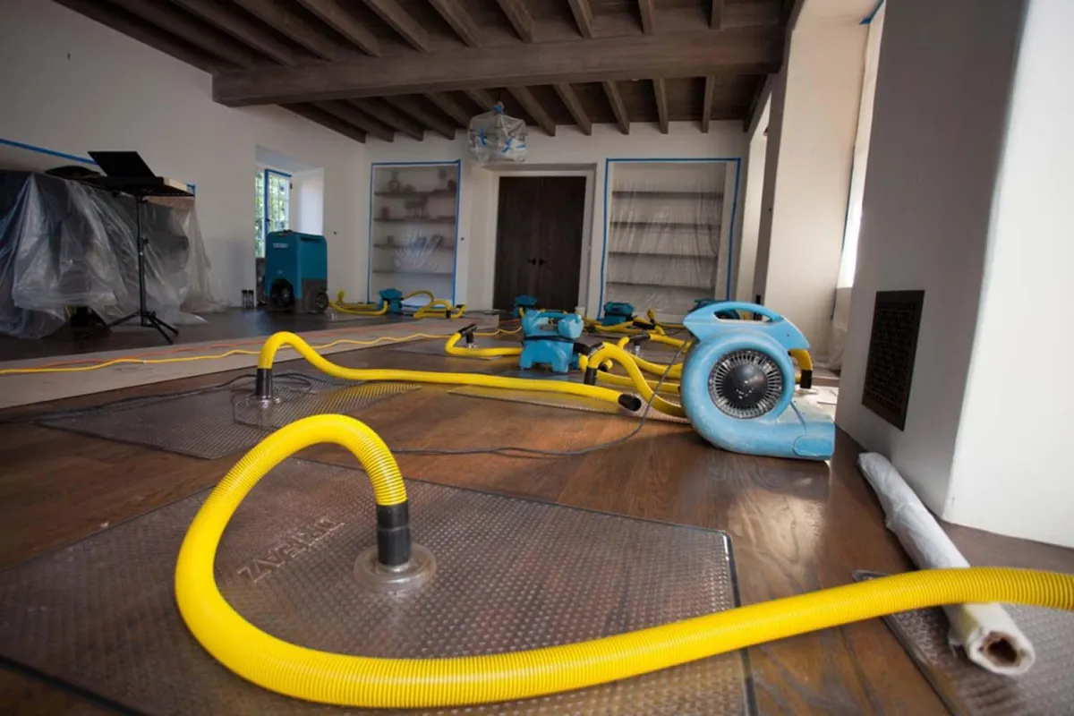 Water damage restoration in progress with dehumidifiers, floor drying system, and industrial fans used by VHrestoration to dry and repair a flooded area.