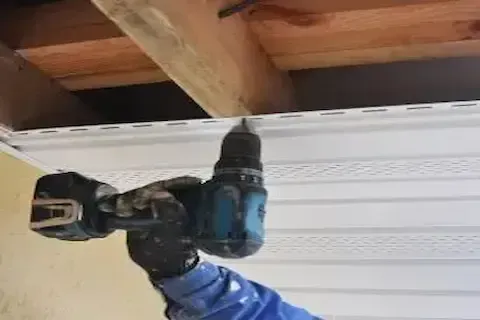 Contractor using power drill to fasten soffit panel during fascia installation by Eden Prairie Roofing