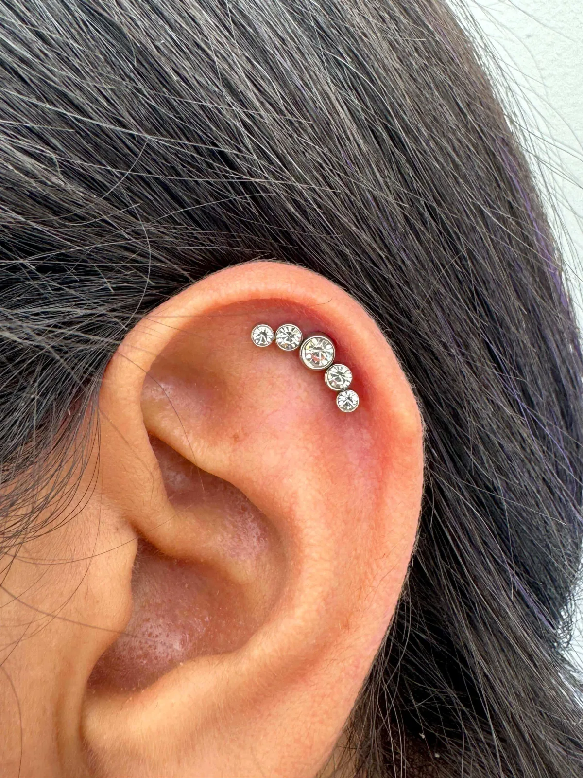 Close-up of an ear featuring multiple cartilage piercings adorned with sparkling gemstones, showcasing a stylish and elegant body modification option offered by GameFace Tattoos.