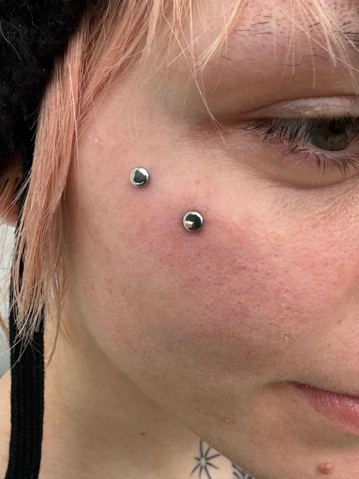 Facial piercings featuring two microdermal implants on the cheek, showcasing a stylish body modification look.