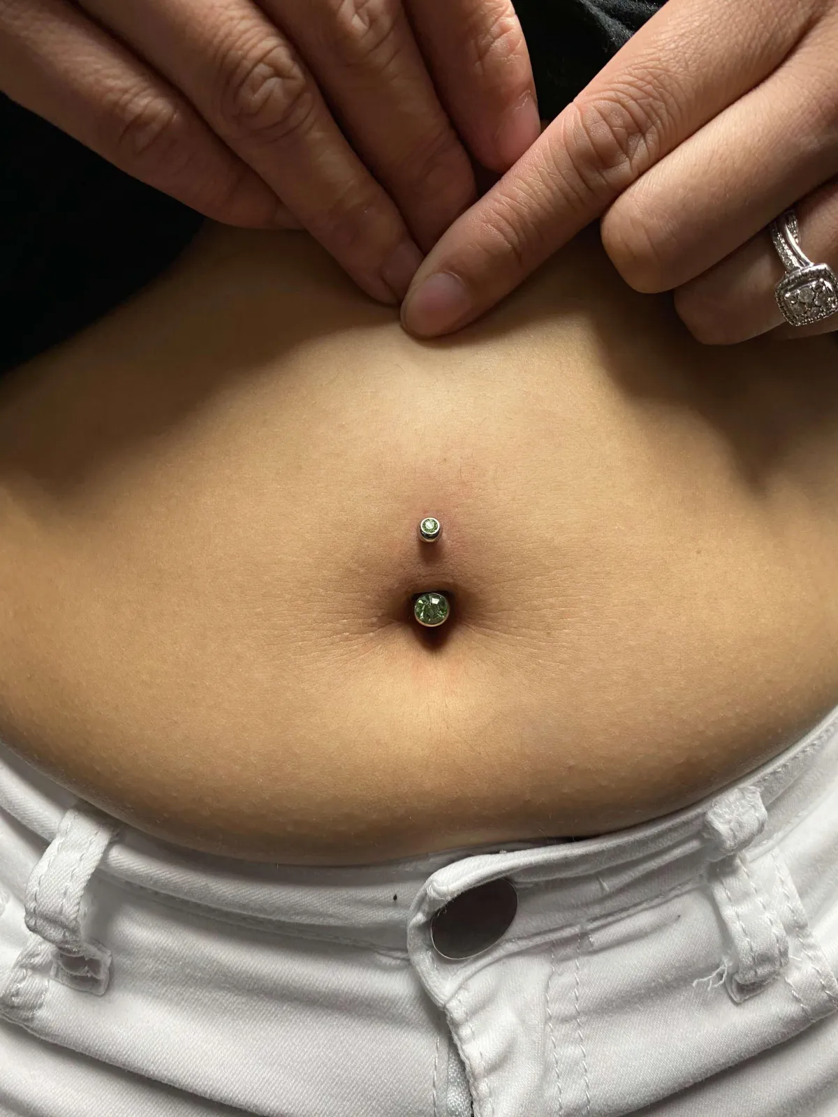 Navel piercing with two decorative jewelry pieces, hands gently touching the area, showcasing professional body modification services at GameFace Tattoos.