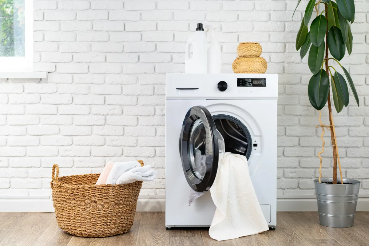 Front-load washer with open door, towels in basket, and laundry supplies on top, symbolizing home appliance maintenance.