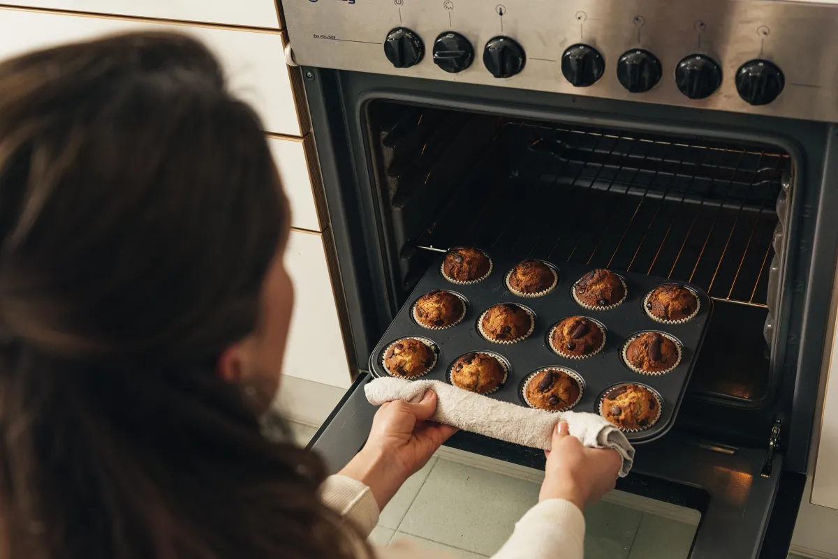 A person removing a tray of freshly baked muffins from the oven symbolizes safe and efficient gas oven repair.