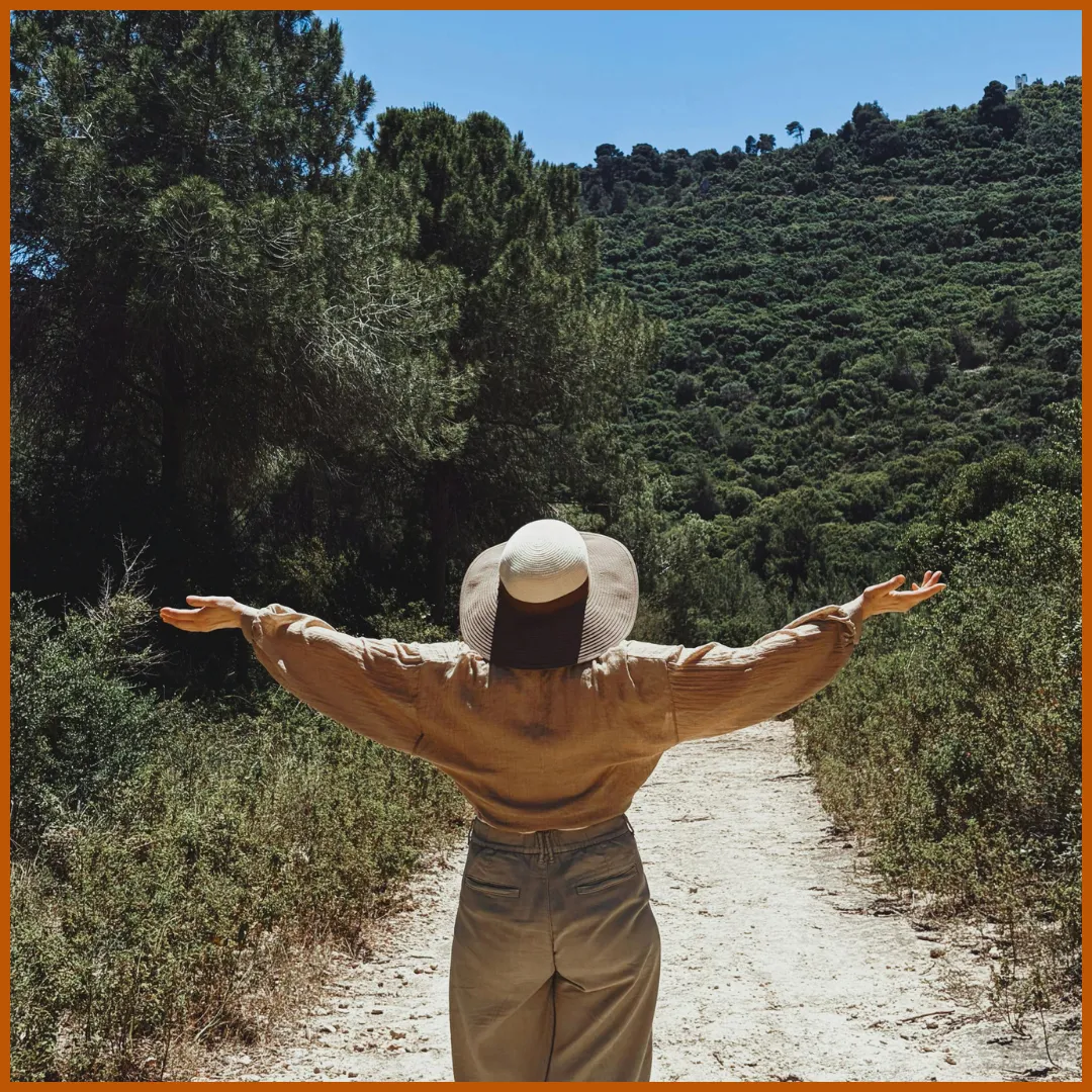 Femme de dos, bras ouvert, face à un sentier en nature