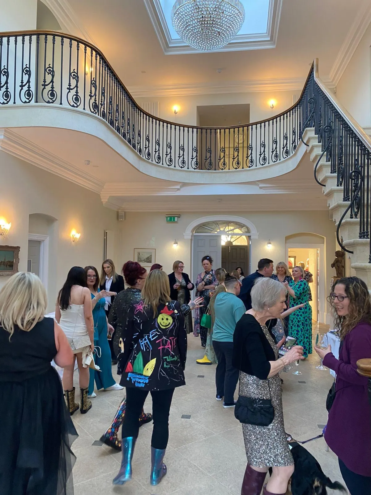 A busy room full of attendees for the welly boot ball with high ceilings and a chandelier at the top of grand stairway at Old Down Manor the venue for the ball