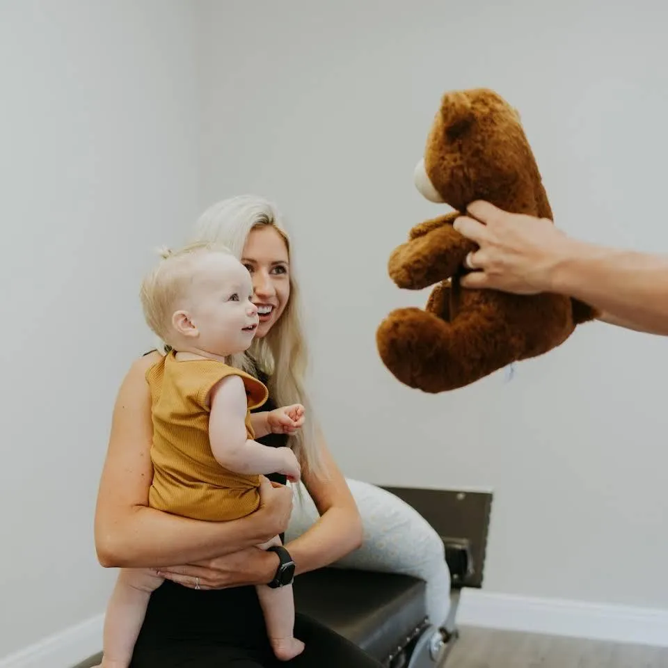 Ao mother and child being comforted by Dr. Brett Grant in a chiropractor office with a teddy bear.