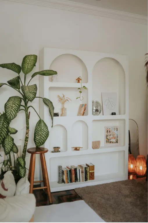 Cozy living room corner with a tall white shelf featuring books, plants, and decor.