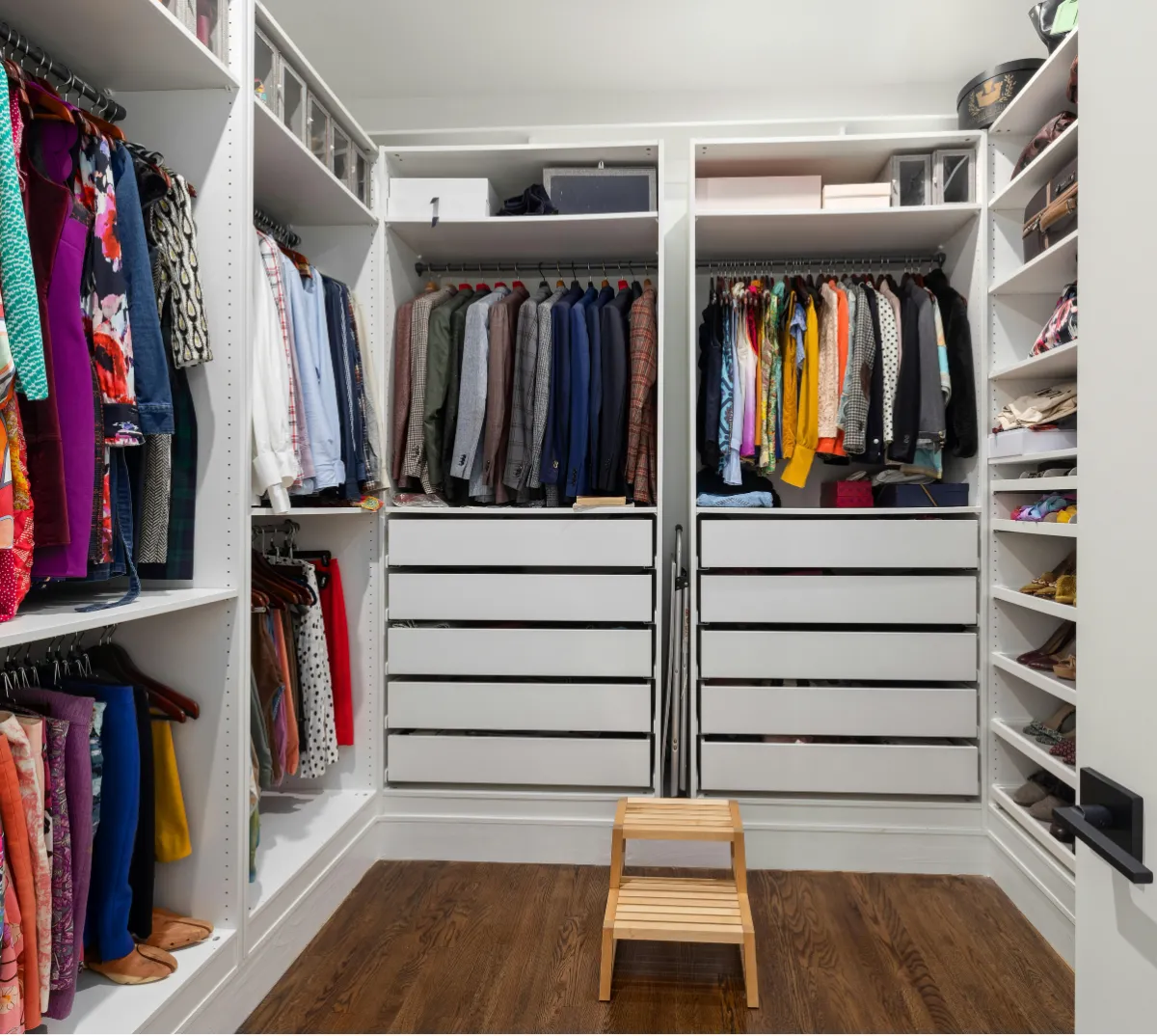A well-organized walk-in closet showcasing a wooden stool and various garments hanging on racks.