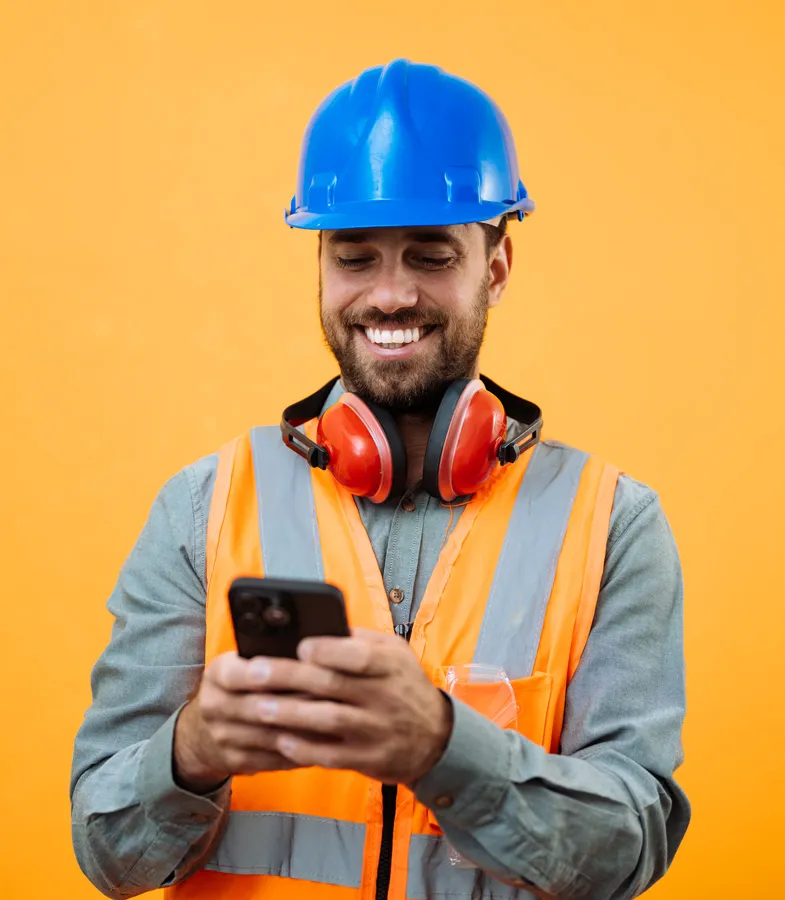 Smiling worker in a hard hat and hi-vis vest checking his phone