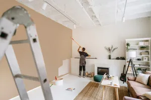 Painter working on a living room wall, with a ladder in the foreground