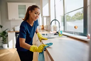 Cleaner in rubber gloves wiping down a kitchen benchtop