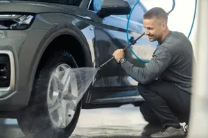 Detailer pressure-washing the wheel of a grey SUV