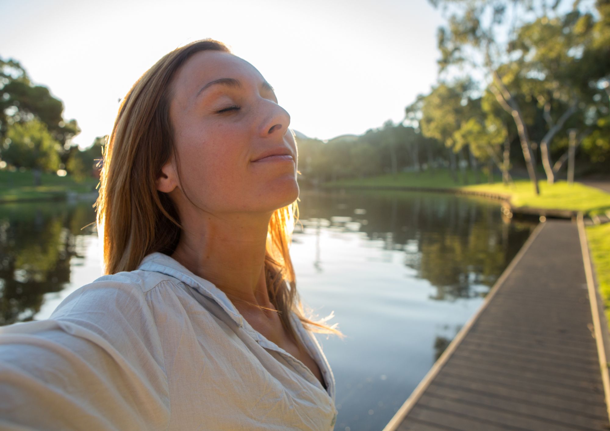 Mind and confidence support for anxiety, fears and procrastination at Pause. Woman closed eyes looking calm and with lake and sun behind