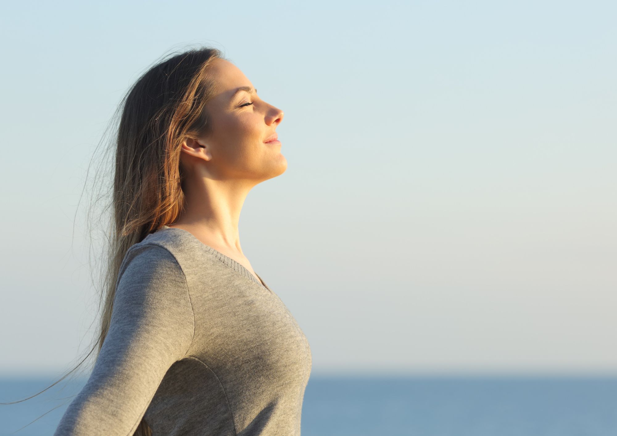 Woman open to receiving calm and wellbeng. Eyes closed facing the sun
