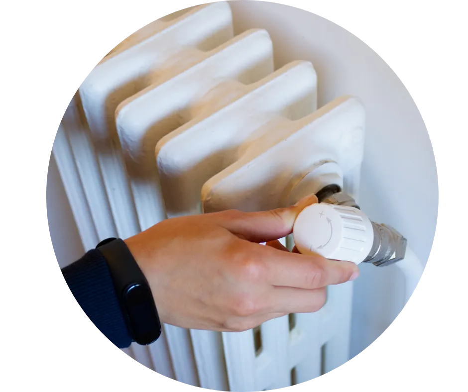 Close-up of a thermostatic radiator valve being adjusted on a traditional white radiator.