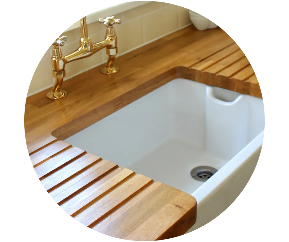 White Belfast-style kitchen sink with traditional brass taps and wooden draining boards, illustrating kitchen plumbing installations and upgrades.