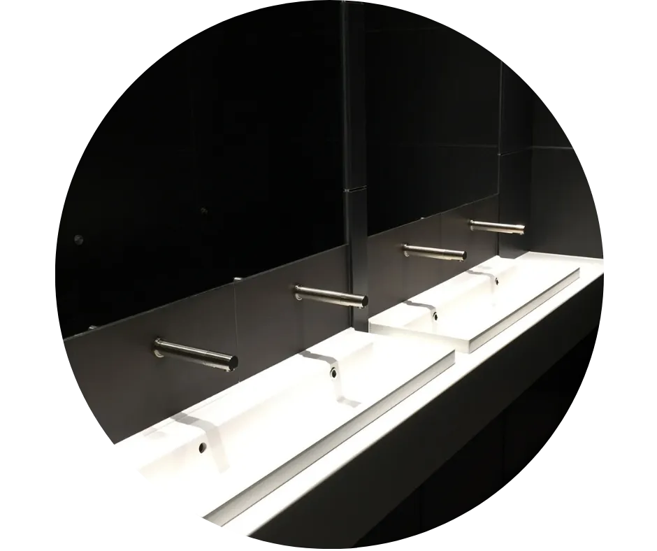 Modern commercial washroom with a row of white basins, wall-mounted taps and dark wall panels. 2. Plumbing for Landlords & Holiday Lets