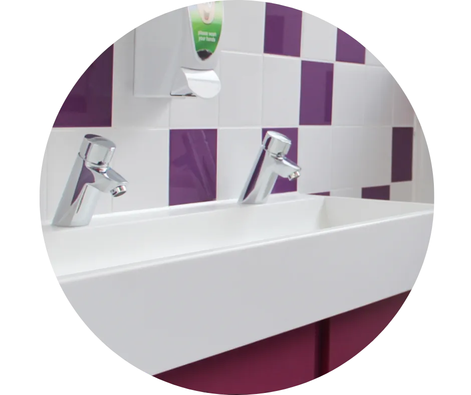 School washroom refurbishment featuring a white trough basin, chrome taps and purple wall tiles, completed by CDI Contractors.