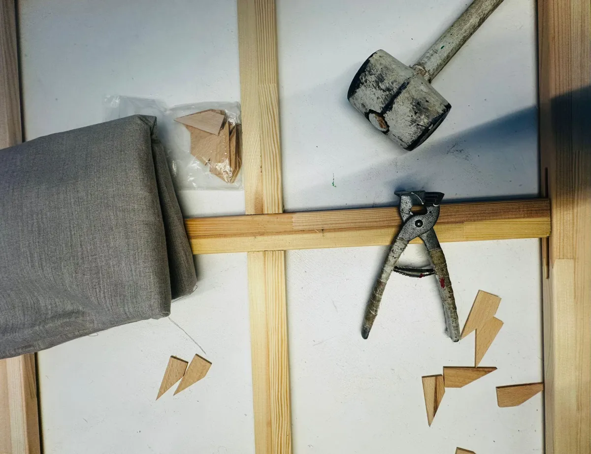 Großer Keilrahmen mit Mittel- und Diagonalsprosse in Montage; Maßband, Keile und Akkuschrauber zeigen Positionierung und Versteifung.