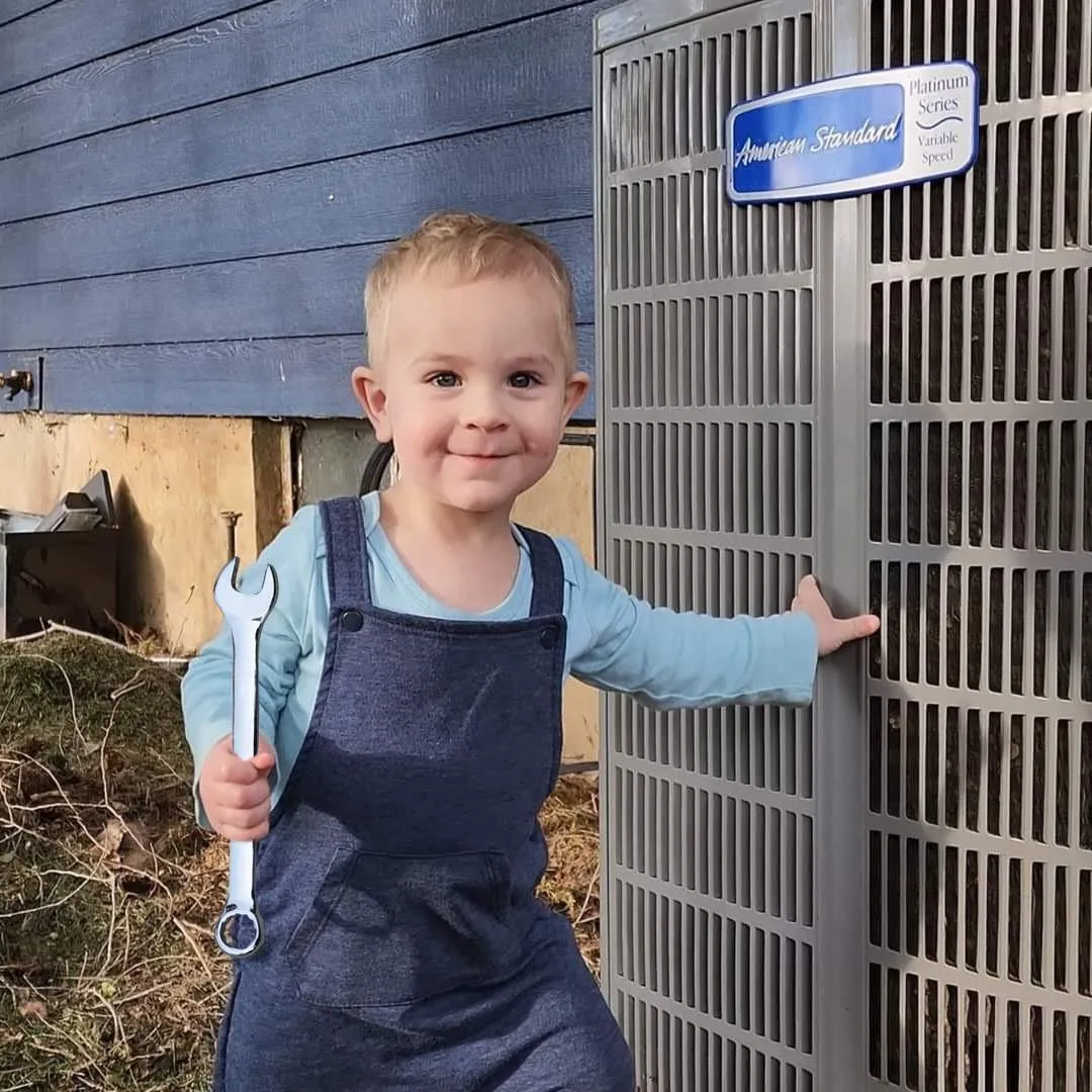 A young boy holds a wrench beside an air conditioner, showcasing his interest in HVAC work at Utah Heating and Air Conditioning.