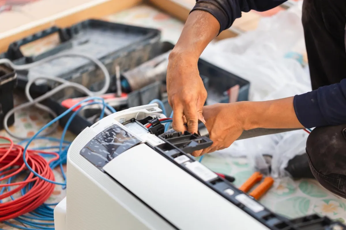 A repairman works on a refrigerator, troubleshooting and connecting various wires inside the unit.