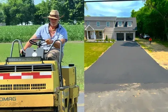 Professional asphalt paving in action: A worker operates a BOMAG 100 AD-2 road roller on a residential driveway. The newly paved driveway leads to a modern two-story home with a neatly maintained front yard. The scene illustrates high-quality asphalt installation and residential driveway paving services.