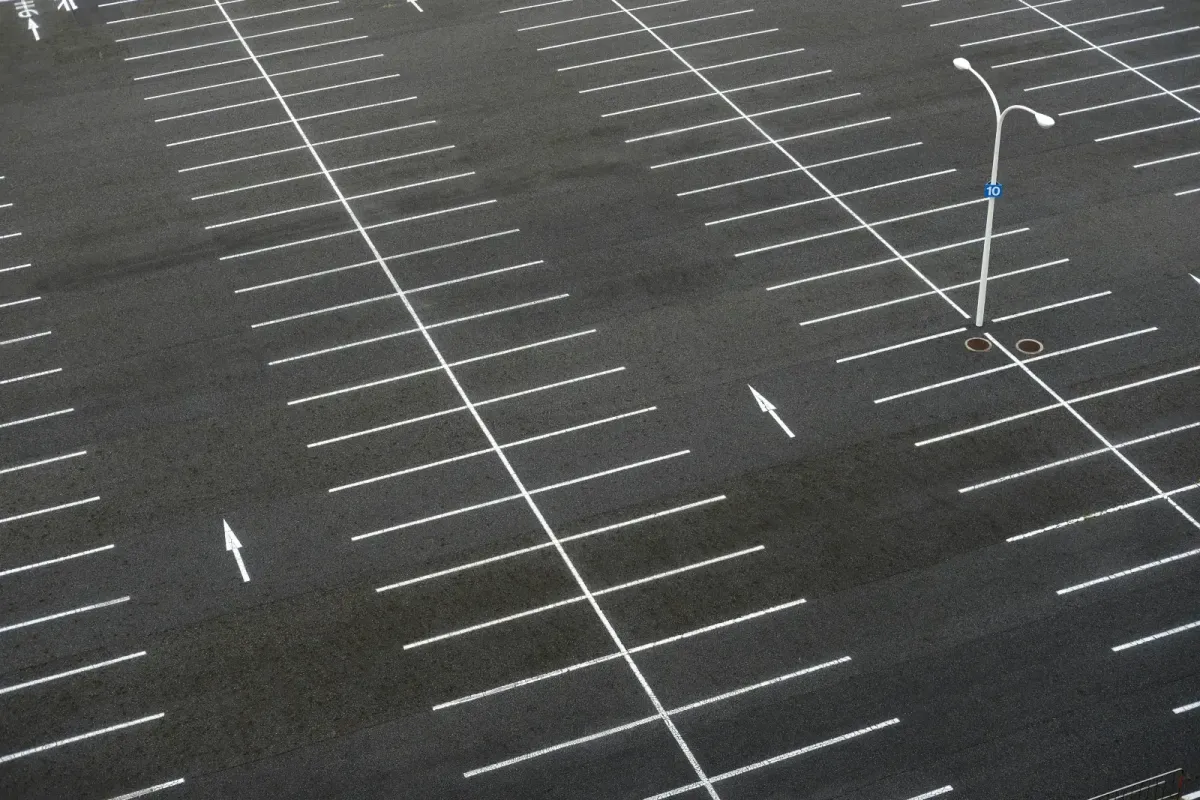 Empty asphalt parking lot with white painted lines, directional arrows, and a single street lamp in the middle.