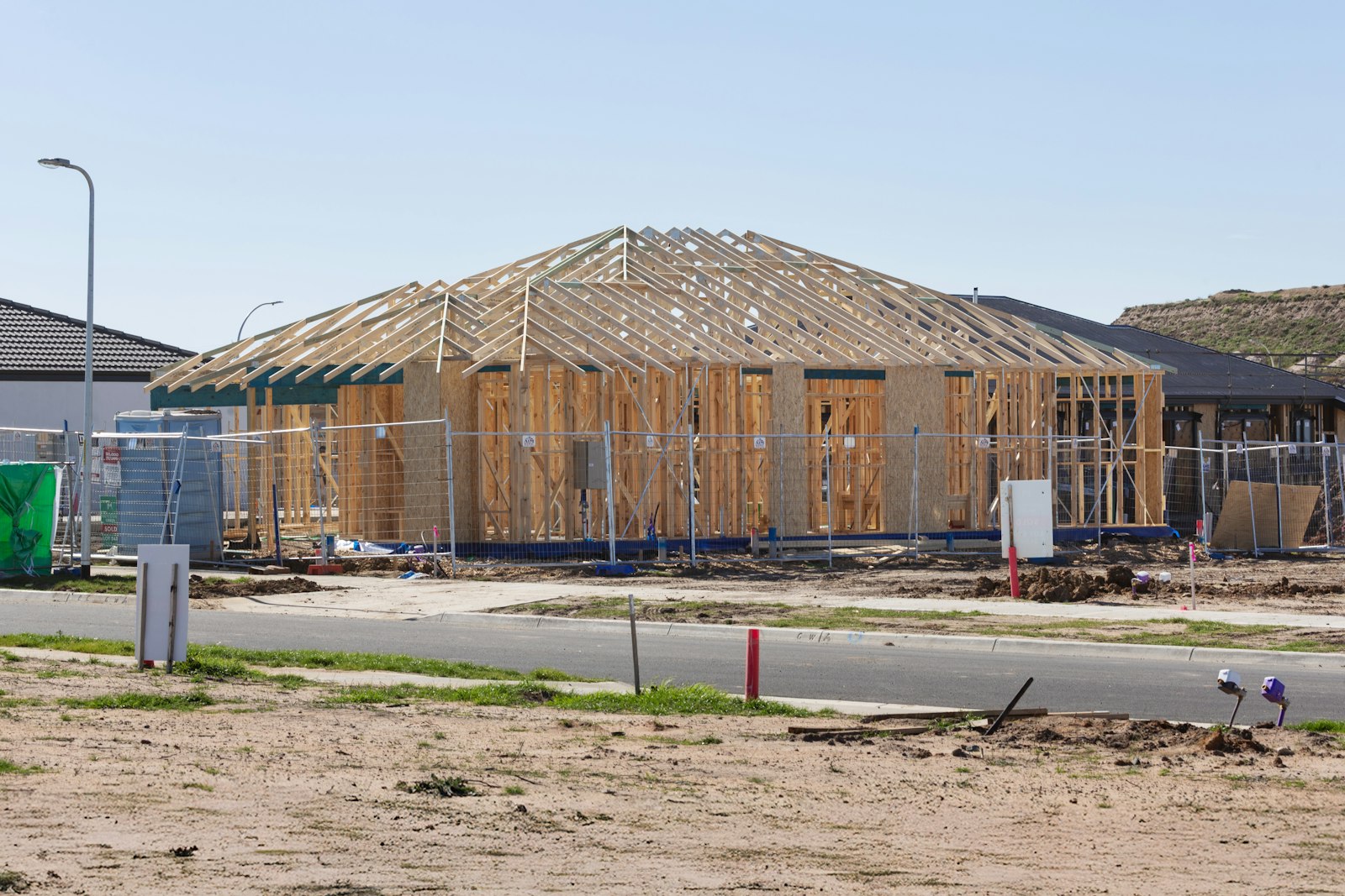 New single-story home framing under construction on a residential lot, roof trusses being installed