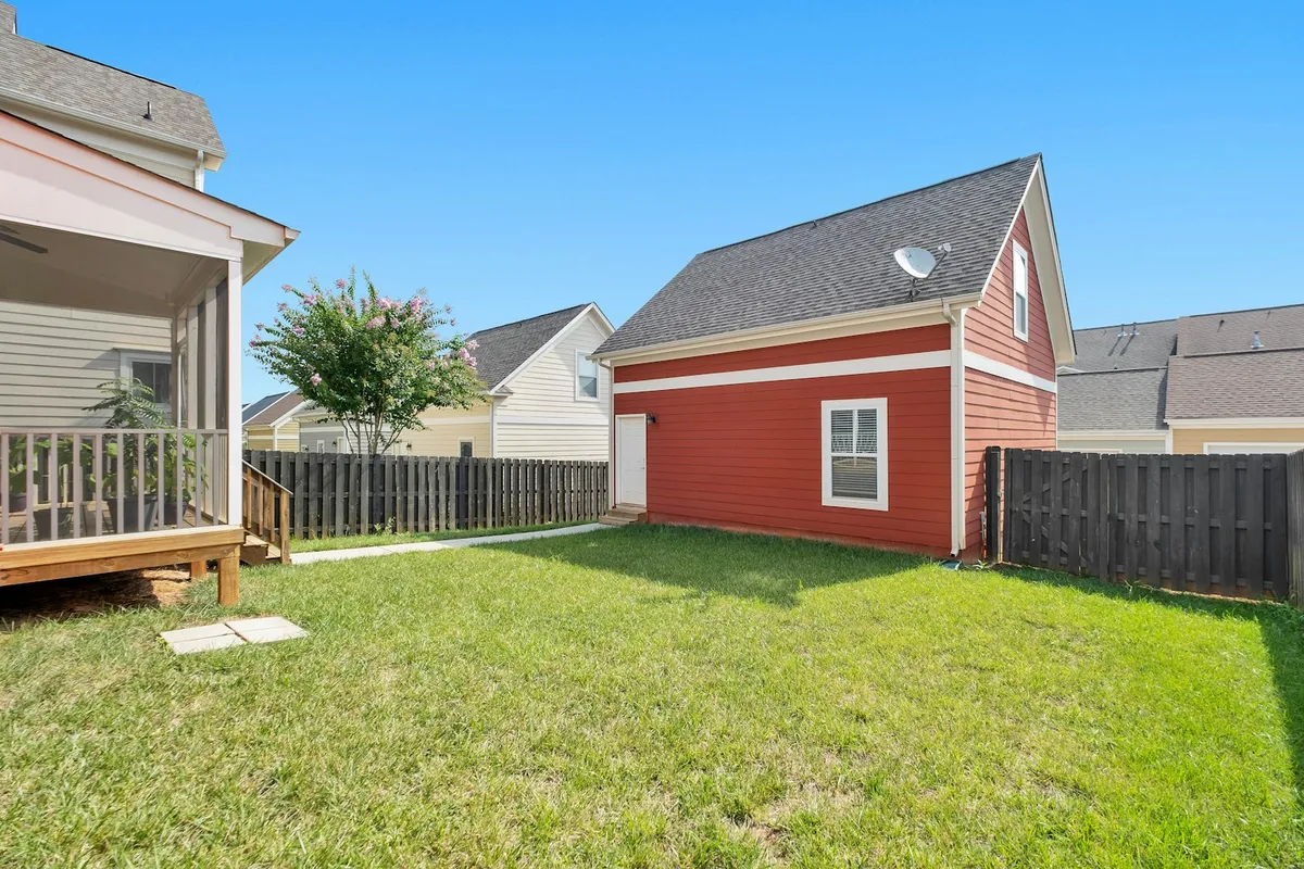 A finished, detached backyard accessory structure with a gable roof and painted siding behind a main home, representing a completed ADU in a residential yard
