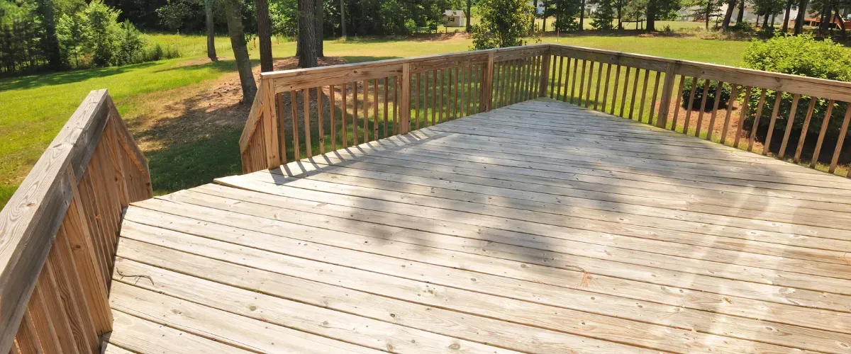 Empty wooden deck in natural finish overlooking grassy backyard area.