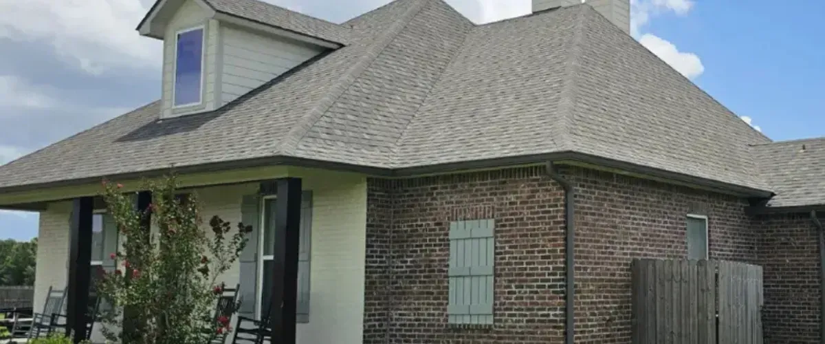 Front view of a suburban home with a light gray shingle roof, brick siding, and covered porch.