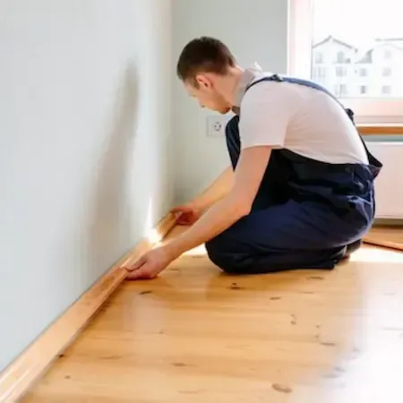 Worker installing skirting board with precision tools, highlighting carpentry and finishing skills.