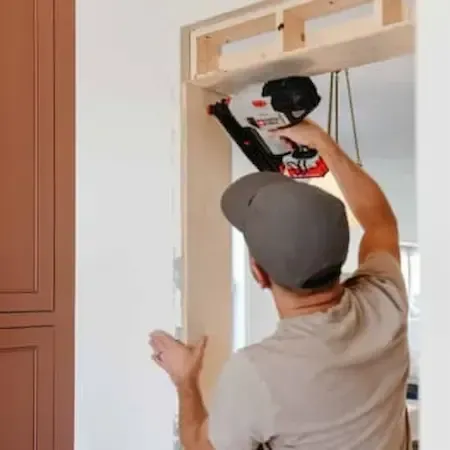 Worker installing door frame with power drill, ensuring hinge alignment and precise fit for carpentry repair work.