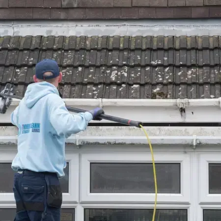 Worker cleaning roof gutter using telescopic pressure washer for mould and debris removal