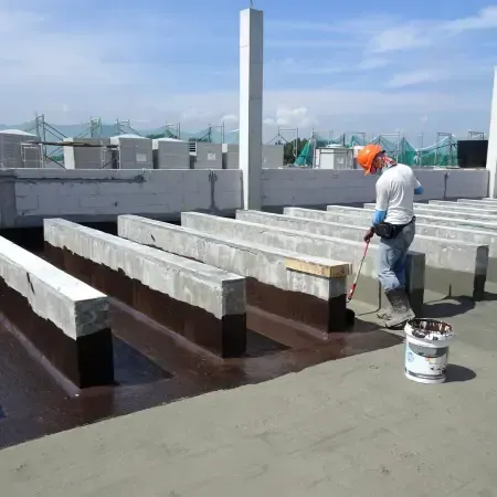Worker applying roof waterproofing sealant on concrete slab with brush for leak prevention