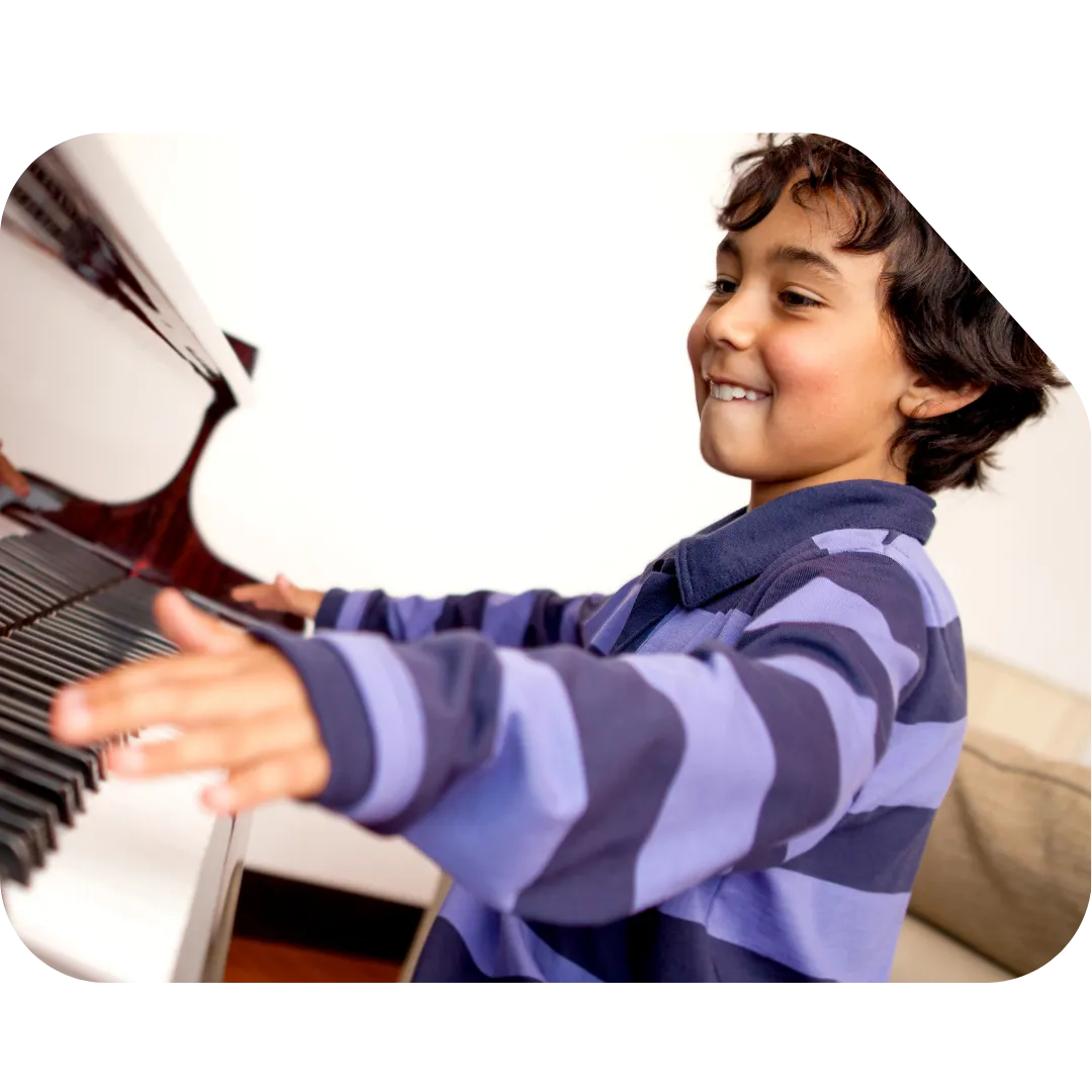 Young boy in a striped shirt smiling while playing a grand piano