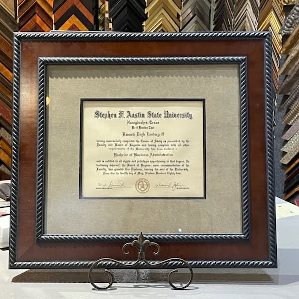 Custom framed Stephen F. Austin State University diploma with double matting and a rich wood frame, professionally displayed on an easel in a custom picture framing showroom.
