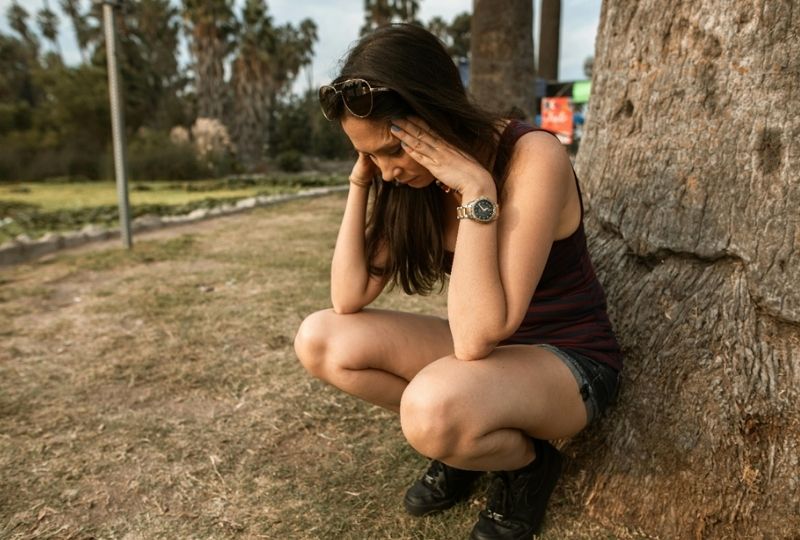 A woman standing beside a tree with her eyes closed and her head slightly bowed.