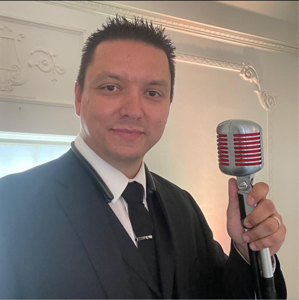 Portrait of DJ OOgo, mid-40s, warm smile, wearing a casual blazer in a cozy Tulsa studio; 1:1 crop, neutral warm background, soft natural light, photorealistic headshot highlighting approachability and professionalism.