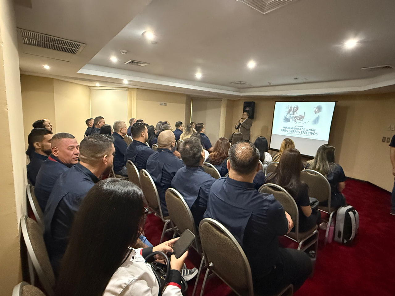 Grupo diverso de profesionales en sala de reuniones, revisando materiales de capacitación, pizarras y laptops, ambiente corporativo, estilo moderno, composición horizontal, fondo claro