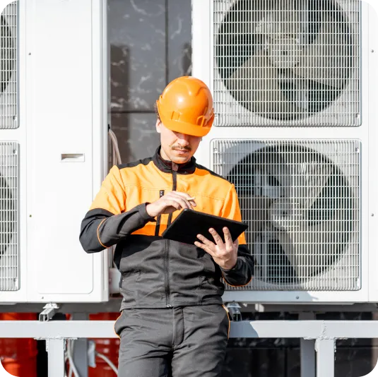 Technician in orange safety gear using a tablet near industrial air conditioning units, emphasizing property maintenance expertise by Priority1 Property Consultants.