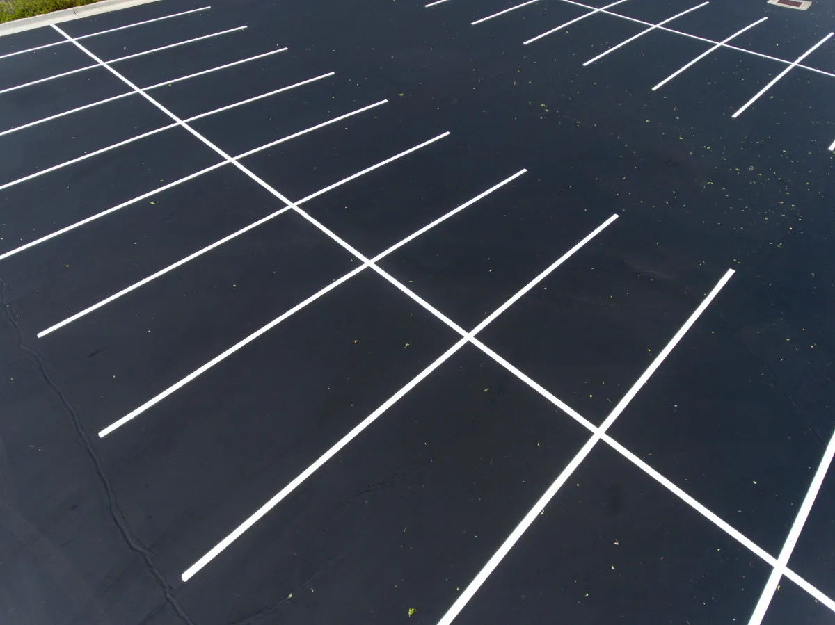 Freshly seal-coated asphalt parking lot with new white line striping and smooth black pavement surface