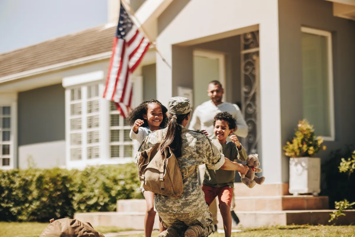 Military parent welcomed home by family outside new house, symbolizing VA loan homeownership.