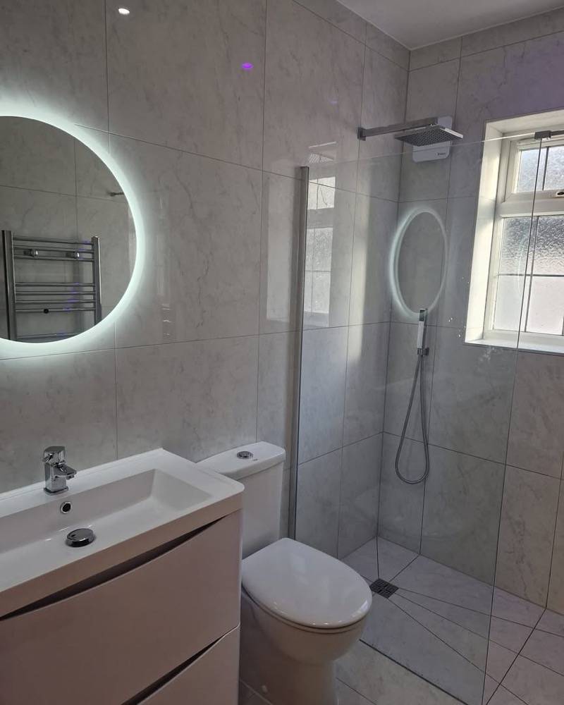 Marble-effect bathroom with round LED mirror and walk-in shower by DR Construction