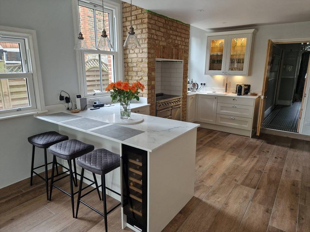 Refurbished kitchen with white marble island and exposed brick wall by DR Construction