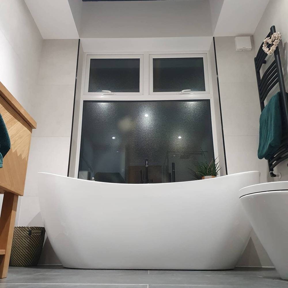 Freestanding bath in white-tiled bathroom by DR Construction